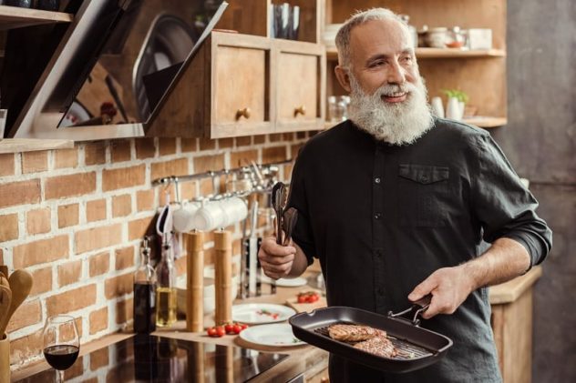 man holding frying pan with steaks