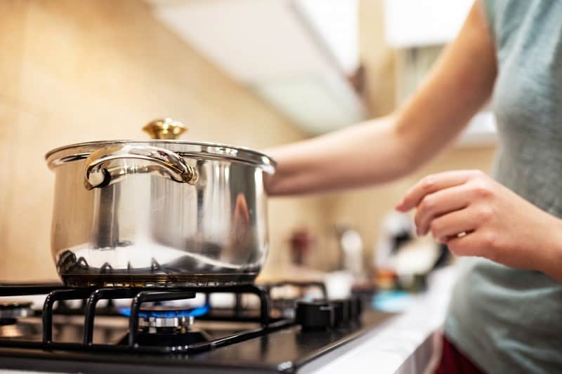 Woman placing steel saucepan on gas hob