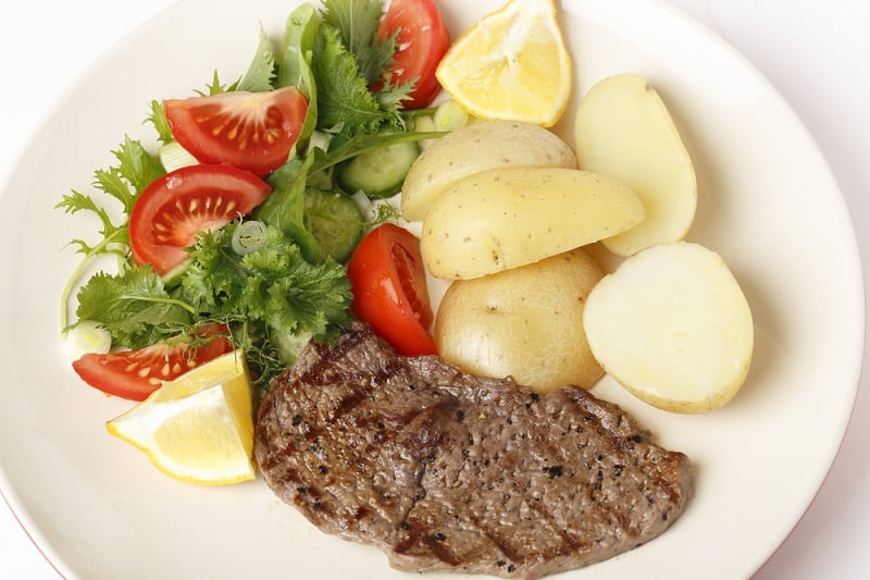 Frying steak on plate with salad and potatoes