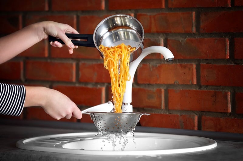 Pasta in colander under tap